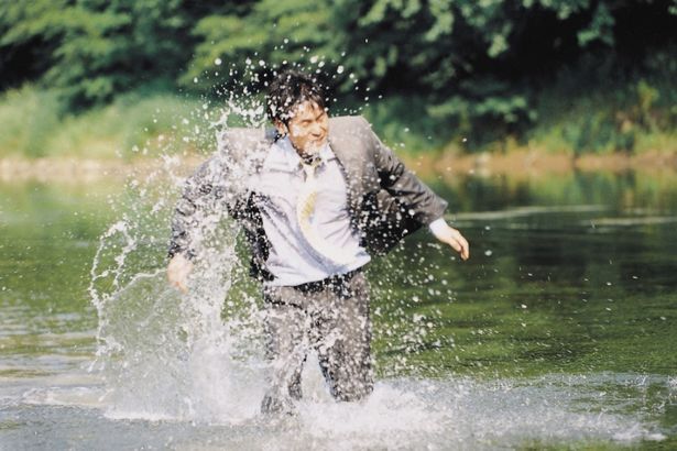 かつてピクニックをした地を訪れたヨンホは、スーツ姿で川に飛び込むなど奇行を繰り返す(『ペパーミント・キャンディー ４Ｋレストア』）